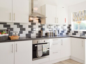 A modern kitchen with white cabinets, black and white tiles, a built-in oven, and a window with a view of greenery.