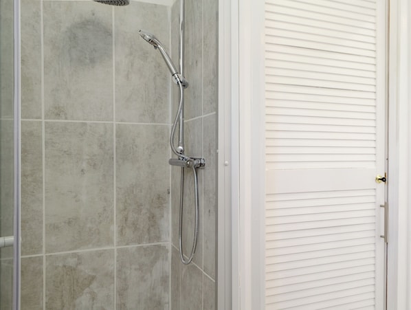 A shower area with a handheld showerhead and a wall-mounted faucet, adjacent to a white door with a gold handle.