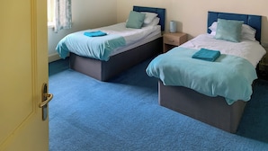 Une chambre avec deux lits, chacun doté d’une tête de lit bleue, d’une table de chevet avec une lampe et d’une fenêtre avec un rideau.