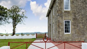 Un bâtiment en pierre avec un portail en métal rouge et une clôture blanche.