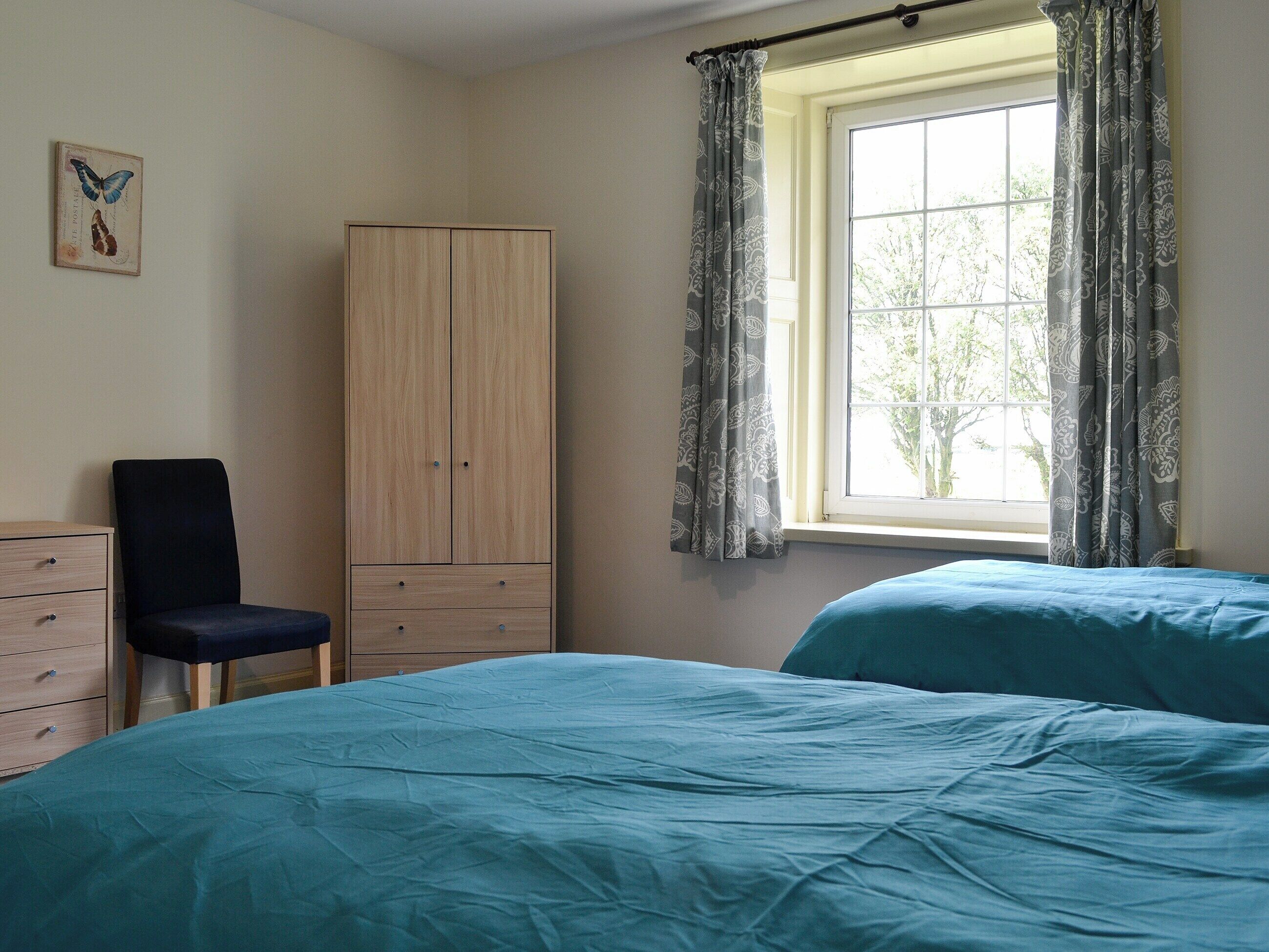 Un dormitorio con dos camas, un armario, una silla y una ventana con cortinas.