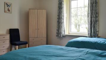 Un dormitorio con dos camas, un armario, una silla y una ventana con cortinas.