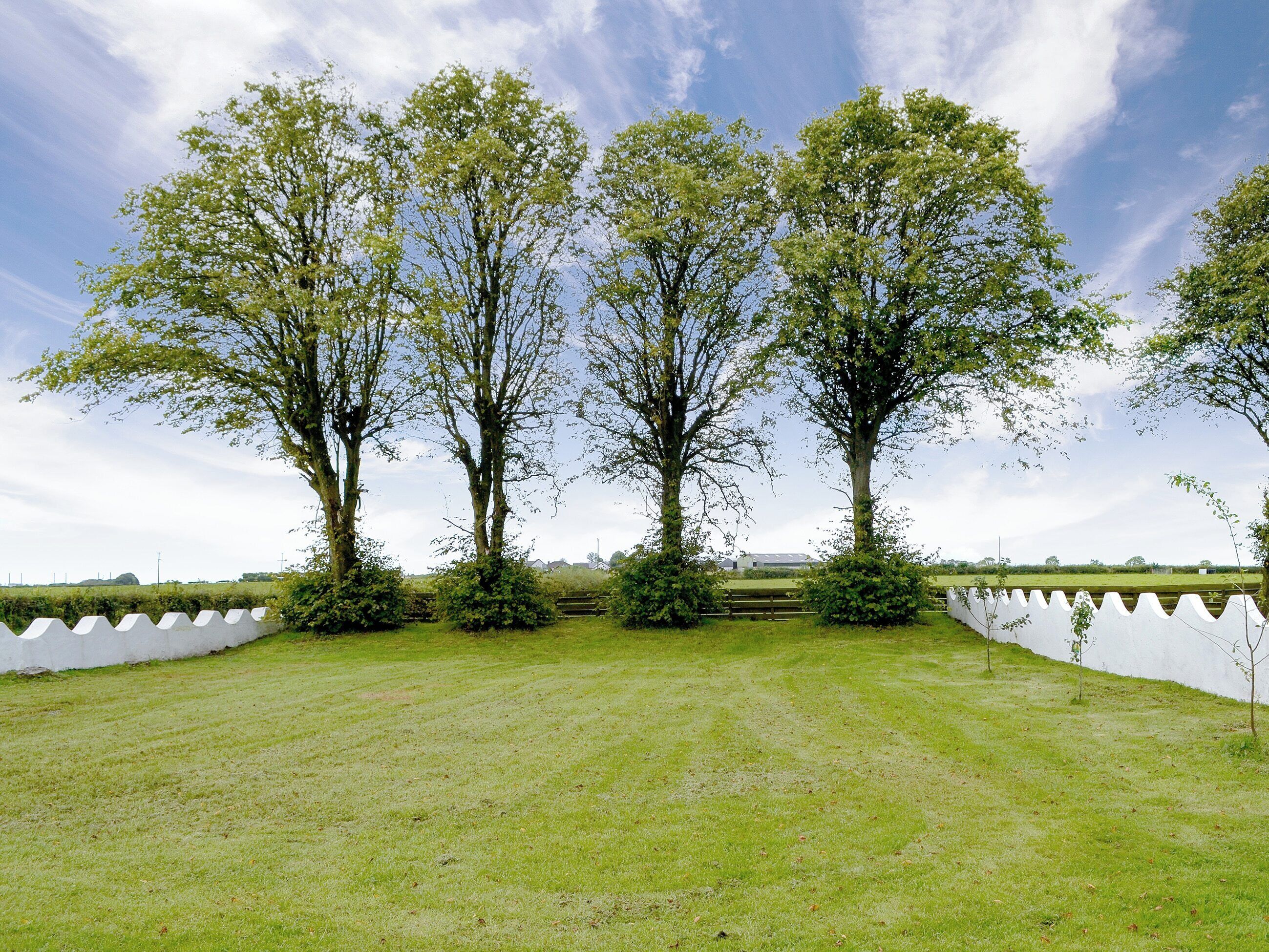 A grassy field with three large trees and a white fence.