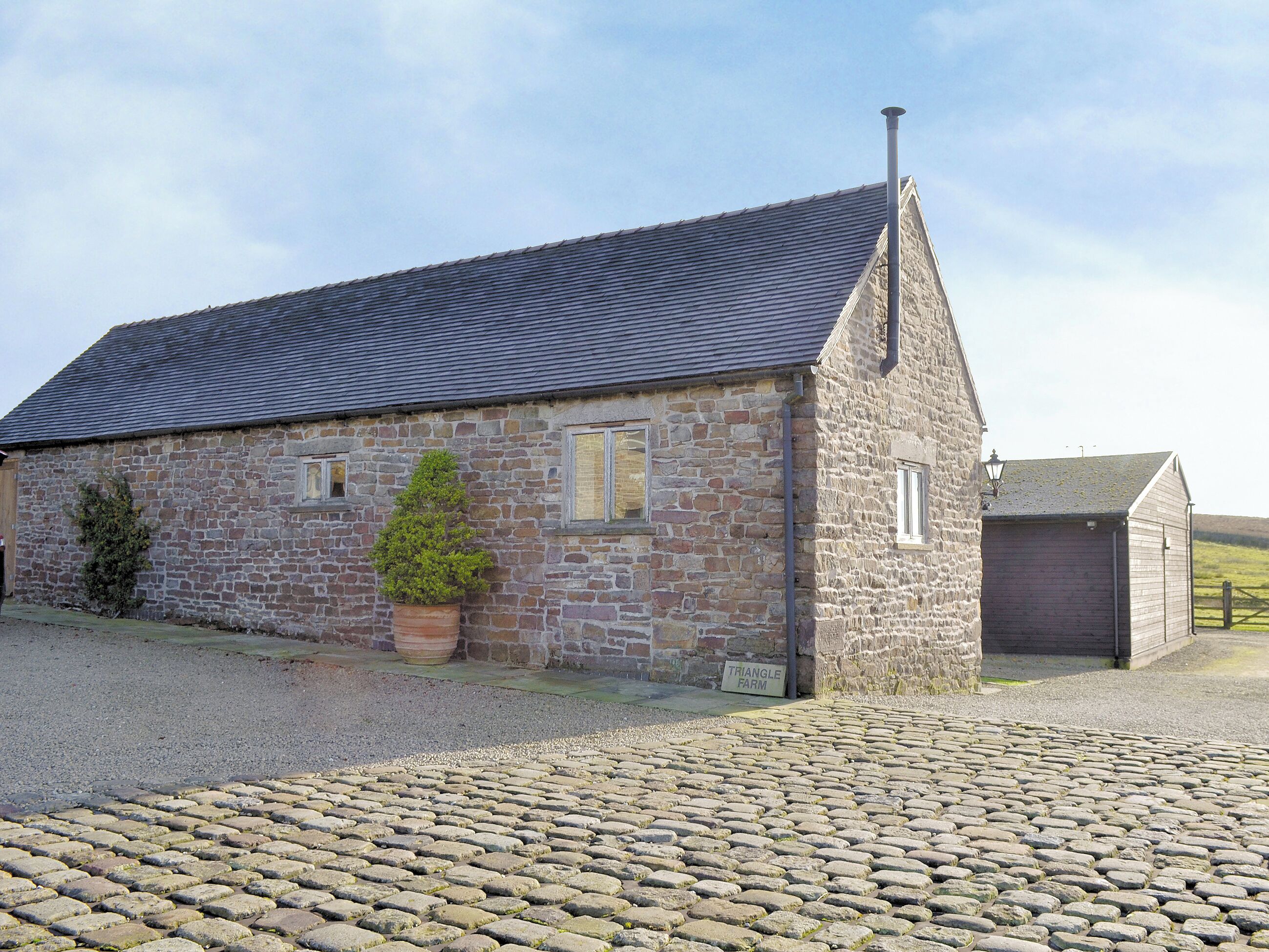 A stone farmhouse with a tiled roof, a potted plant, and a gravel driveway.