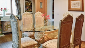 Un comedor con una mesa de vidrio rodeada de sillas ornamentales, una araña y obras de arte en las paredes.