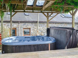 A hot tub under a wooden pergola with stone walls and a window. - Charming barn conversion with hot tub and walks from the door. (Ymwlch, near Porthmadog)