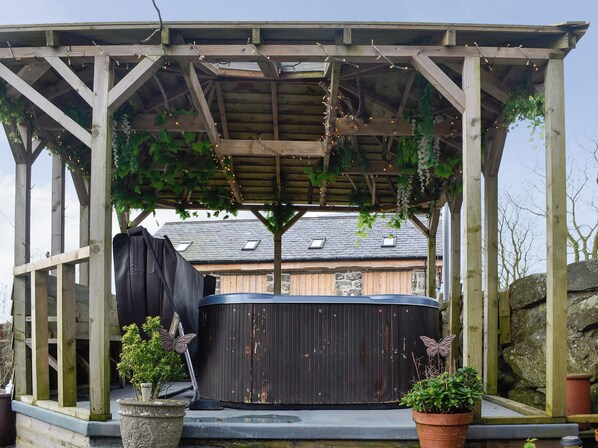 Un belvédère en bois abritant un jacuzzi, entouré de plantes en pot et d’un mur de pierres.