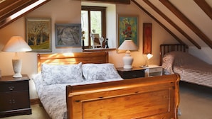 Un dormitorio con una cama de madera, dos mesitas de noche, una ventana con vistas y obras de arte en las paredes.