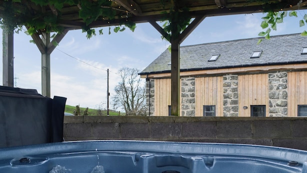 Un jacuzzi con una pared de piedra y un edificio de madera al fondo.