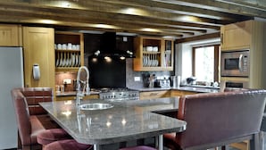 Una cocina moderna con una isla central, taburetes de bar, electrodomésticos de acero inoxidable y armarios de madera.