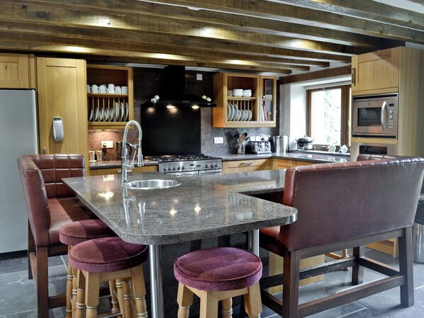 A modern kitchen with a central island, bar stools, stainless steel appliances, and wooden cabinetry. - Charming barn conversion with hot tub and walks from the door. (Ymwlch, near Porthmadog)