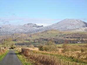 Une route de campagne qui mène à un paysage montagneux, sous un ciel dégagé.