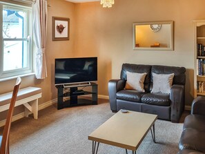 A living room with a television, leather sofa, a small table, a bookshelf, and a window with curtains.