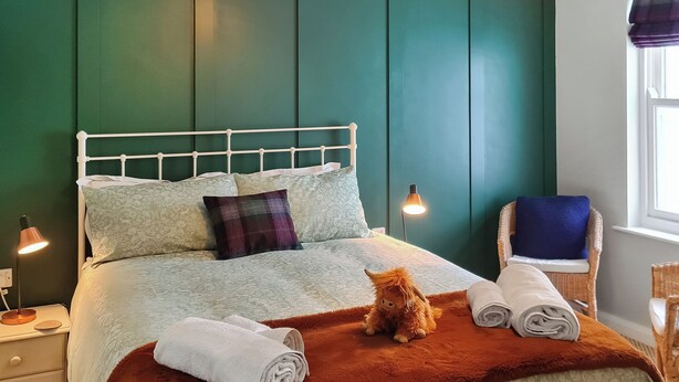 A bed with a headboard, pillows, a blanket, a teddy bear, and rolled towels. - 2 bedroom accommodation in Keswick (Keswick)