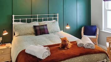 A bed with a headboard, pillows, a blanket, a teddy bear, and rolled towels.