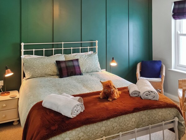 A bed with a headboard, pillows, a blanket, a teddy bear, and rolled towels.