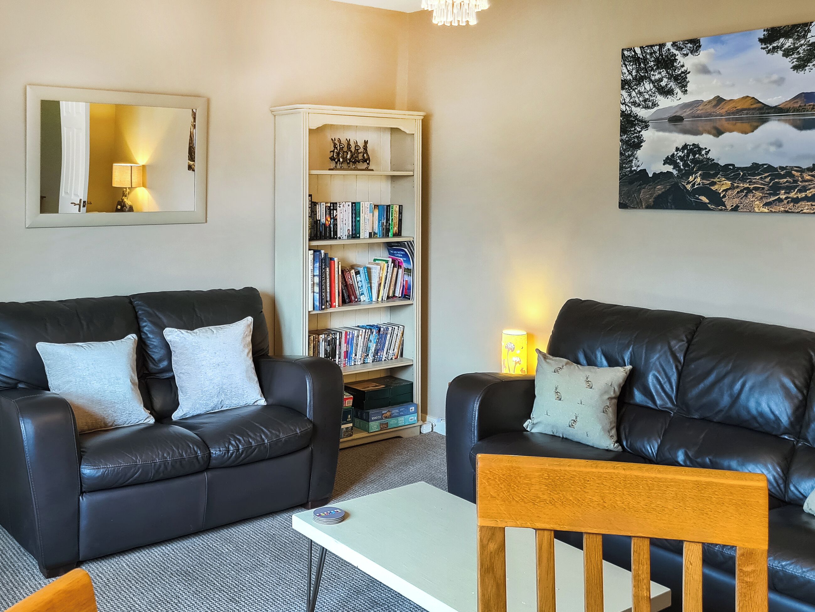 A living room with two black leather sofas, a wooden coffee table, a bookshelf, and a painting of a landscape.