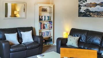 A living room with two black leather sofas, a wooden coffee table, a bookshelf, and a painting of a landscape.