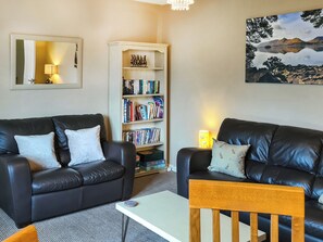 A living room with two black leather sofas, a wooden coffee table, a bookshelf, and a painting of a landscape.