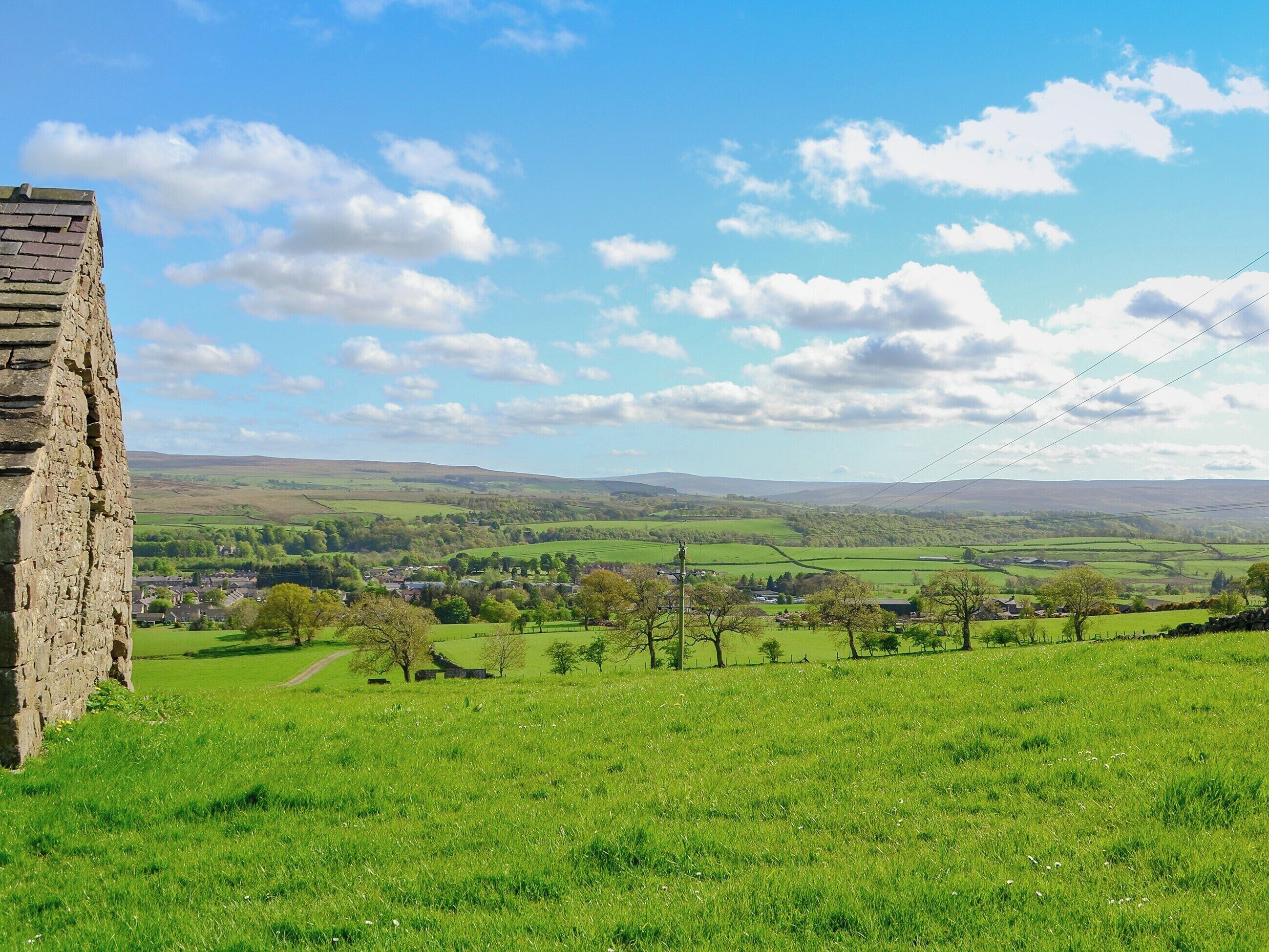 A stone structure in a green field with a village in the distance.