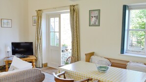 Una habitación acogedora con una mesa a cuadros, muebles de mimbre, televisión y ventana con cortinas.