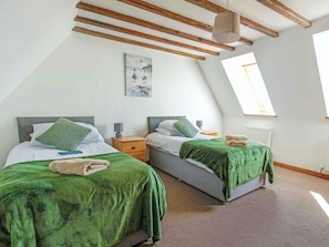 Een kamer met twee bedden, elk met een groene plaid en kussens, een houten plafond, een schilderij aan de muur en een raam met uitzicht.