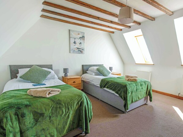 A room with two beds, each with a green bedspread and pillows, a wooden ceiling, a painting on the wall, and a window with a view.