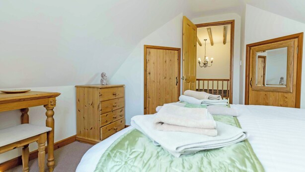 Een slaapkamer met een bed, een houten dressoir, een bureau en een spiegel.