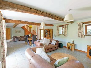 A spacious living area with a high ceiling, exposed wooden beams, a dining table with chairs, a sofa, and a small side table.