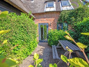 A brick building with a thatched roof, a wooden bench, and a well-maintained hedge.