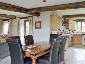 Un coin repas avec une table en bois et des chaises noires, une cuisine avec des meubles en bois et une fenêtre avec des rideaux.