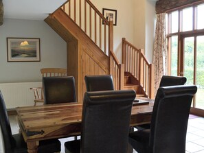 Un comedor con mesa y sillas de madera, una escalera y un ventanal con cortinas.