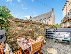 A stone wall with a sign reading "Captain's Corner," a wooden table with plates and glasses, and a bench with cushions.