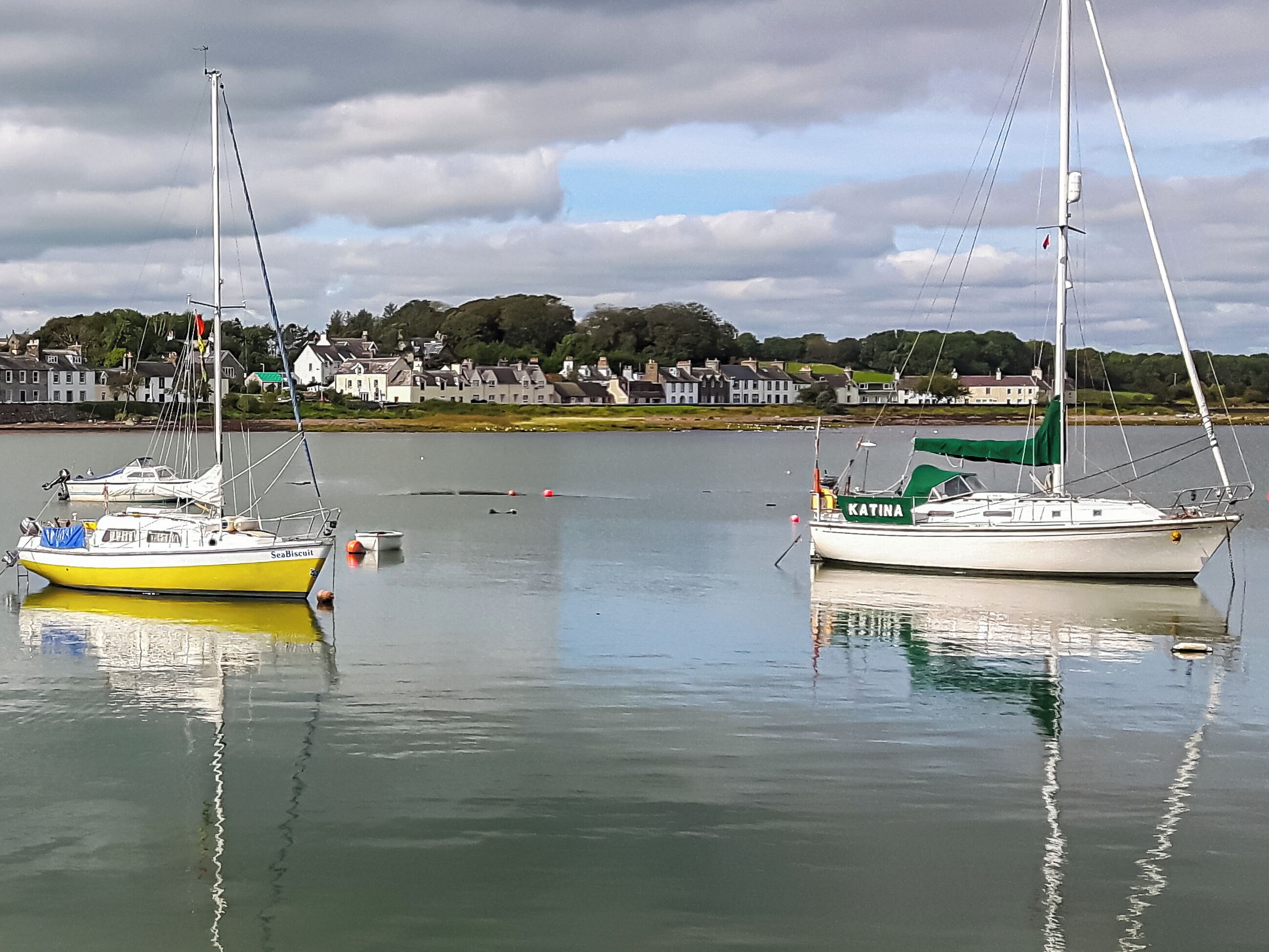 Two sailboats docked at a calm harbor with a town in the background.