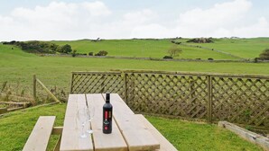 Een picknicktafel met een fles en glazen, voor een achtergrond van een grasveld en een stenen muur.