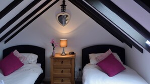 Een slaapkamer met twee bedden, een nachtkastje met een lamp, een spiegel in de vorm van een hart en een houten dressoir.
