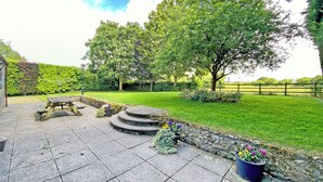 A patio area with a wooden table and benches, surrounded by a stone wall and potted plants.