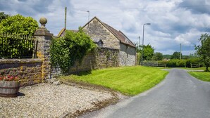 A stone house with a sloped roof, a gravel driveway, and a grassy area with a fence.