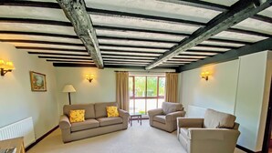 A living room with a high ceiling, exposed beams, and a large window with curtains. There are two sofas and a small table.