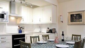 A modern kitchen with white cabinets, a microwave, and a toaster. There is a dining table set with plates, glasses, and a bottle of wine. - Inverchroskie Cottage (Enochdhu, near Pitlochry)