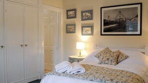 A hotel room with a bed, a nightstand with a lamp, a wardrobe, and framed pictures on the wall. - Inverchroskie Cottage (Enochdhu, near Pitlochry)