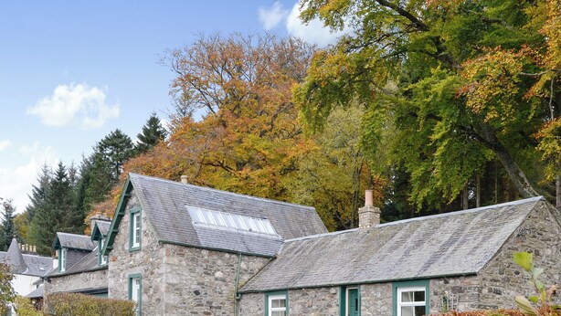 A stone house with a sloped roof and a chimney, surrounded by autumn foliage and a hedge. - Inverchroskie Cottage (Enochdhu, near Pitlochry)