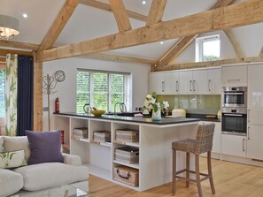 A kitchen with wooden beams, white cabinets, a built-in island, and a dining area with a wicker chair. - 1 bedroom accommodation in St Blazey, near Par (St Blazey, near Par)