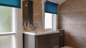 A bathroom with a toilet, a sink with a mirror, and a window with a blue valance. - 3 bedroom accommodation in Keswick (Keswick)