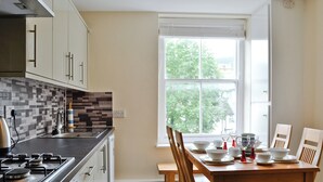 A modern kitchen with a dining area, featuring a large window, a stove, and a dining table set for four. - 3 bedroom accommodation in Keswick (Keswick)