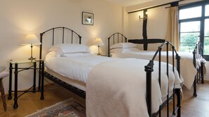 A bedroom with two beds, a nightstand with a lamp, a framed picture on the wall, and a window with curtains. - Parker’s dates from 1610 and is part of the 700-acre Netherley Hall Estate. (Mathon, near Malvern)