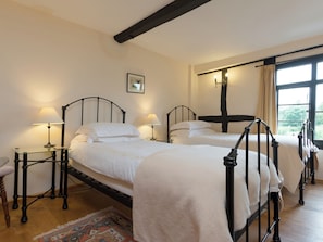 A bedroom with two beds, a nightstand with a lamp, a framed picture on the wall, and a window with curtains. - Parker’s dates from 1610 and is part of the 700-acre Netherley Hall Estate. (Mathon, near Malvern)