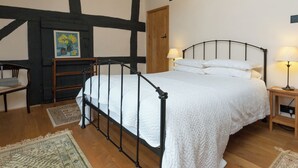 Een slaapkamer met een hemelbed, een houten stoel, een schilderij, een kroonluchter en een nachtkastje met een lamp.