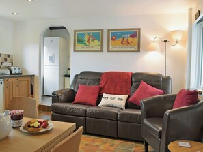 Ein Wohnzimmer mit einem braunen Ledersofa, einem Esstisch mit Erdbeeren und Marmelade und zwei gerahmten Postern an der Wand.