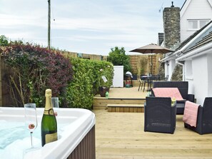 A hot tub with a bottle of champagne and a glass, surrounded by outdoor furniture and a wooden deck. - 2 bedroom accommodation in Johnston, near Broad Haven (Johnston, near Broad Haven)